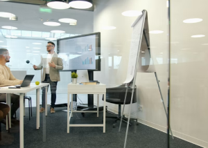 Wall-mounted screen showing a sales bar chart next to a blank flip chart in an office